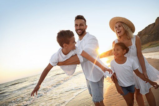 Happy family having fun on sandy beach near sea at sunset.